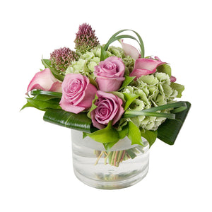 Flower arrangement featuring pink roses, green hydrangeas, pink calla lilies & allium arranged in a clear glass vase, in Flower Studio's signature style.