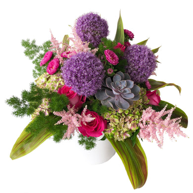 Arrangement featuring purple allium, pink hydrangea, pink astilbe, pink flowers, green leaves, and succulents arranged in Flower Studio style in ceramic white vase.