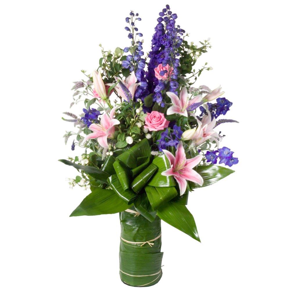 Tall flower arrangement featuring pink lilies, pink roses, purple stocks, premium greenery in a clear glass vase with green leaf wrap arranged in Flower Studio signature style. 